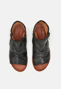 Zapatos negros de piel deslizables con suelas de cuero marrón, que presentan un diseño superior fruncido y una cremallera lateral. Textura suave y puntera redondeada.