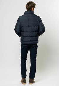 Marineblå boblejakke med høy krage og horisontalt quiltet mønster, parret med mørke jeans og brune støvler. Glatt tekstur, lett design.