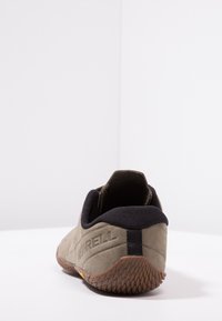 Une chaussure Merrell beige vue de derrière, avec une semelle marron texturée et un col rembourré noir, sur une surface et un fond blancs unis.