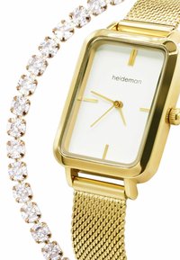Goldenes rechteckiges Armband mit einem weißen Zifferblatt und goldenen Zeigern, das ein Netzband aufweist. Daneben befindet sich ein Strassarmband mit runden, klaren Steinen.
