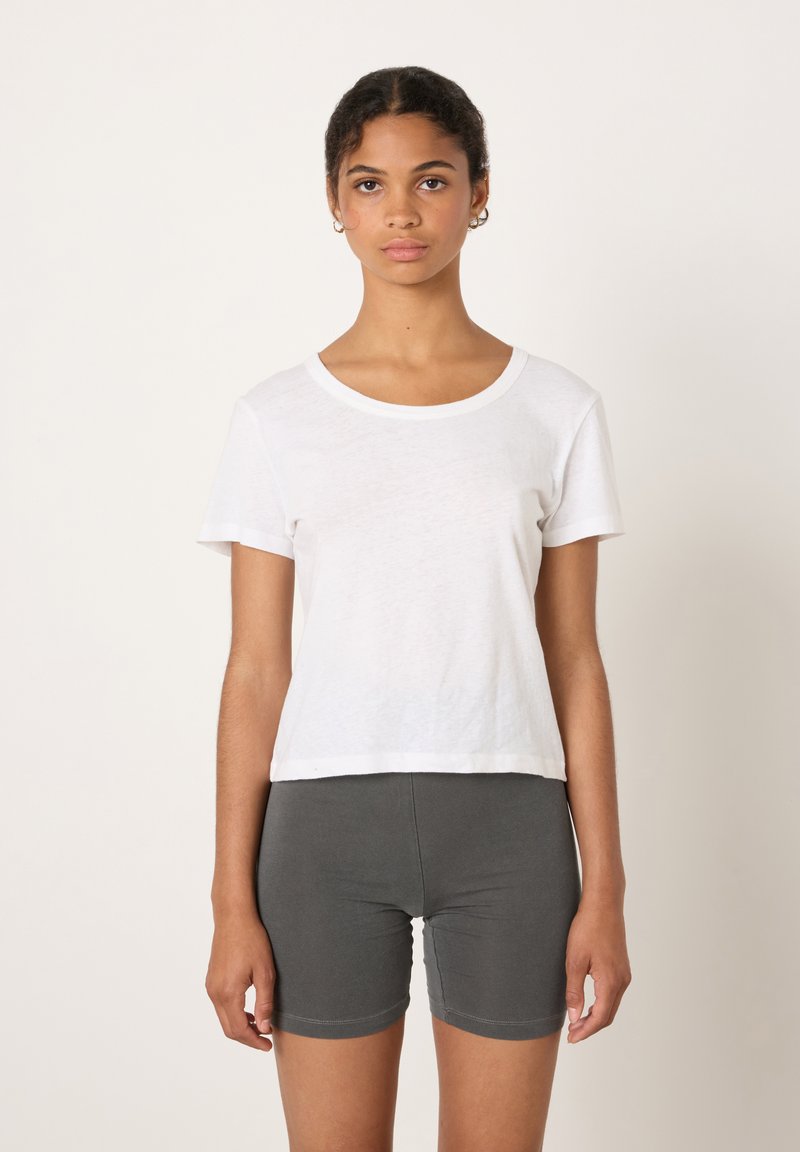 Weißes kurzärmliges T-Shirt mit rundem Halsausschnitt und lockerer Passform, kombiniert mit grauen, eng anliegenden Shorts. Schlichtes Design, weiche Textur.