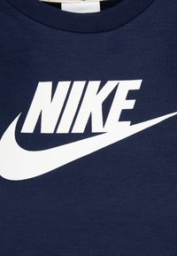 T-shirt en coton bleu marine avec un grand logo blanc "NIKE" et un design de swoosh simplifié à l'avant. Forme classique à col rond.