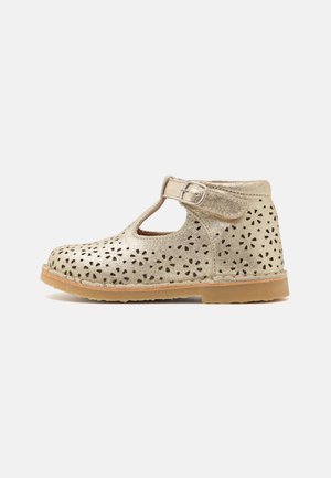 Scarpa in pelle perforata dorata con design a T e fibbia regolabile, dotata di suola in gomma color testa di moro e motivi floreali intagliati.