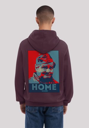 Maroon hoodie featuring a graphic of a man with a hat, highlighted in red and blue, with the text "HOME GUARD" below the image.