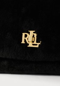 Czarna torebka z pluszu z złotym metalowym zapięciem w kształcie logo "RL". Tekstura wydaje się miękka i puszysta, o wyraźnie zdefiniowanym prostokątnym kształcie.
