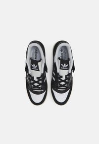 Zwart-witte sport schoenen met een bovenwerk van suède en mesh, geperforeerde teenbox en drie-strepen branding aan de zijkanten. Rubberen zool.