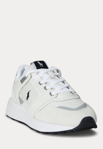 Baskets blanches de sport avec logo noir, lacets blancs et semelle texturée, inclinées vers la gauche sur un fond blanc uni.