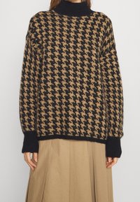 Zwart- en tan houndstooth gebreide trui met geribde manchetten en zoom, gedragen met een beige geplooide rok.