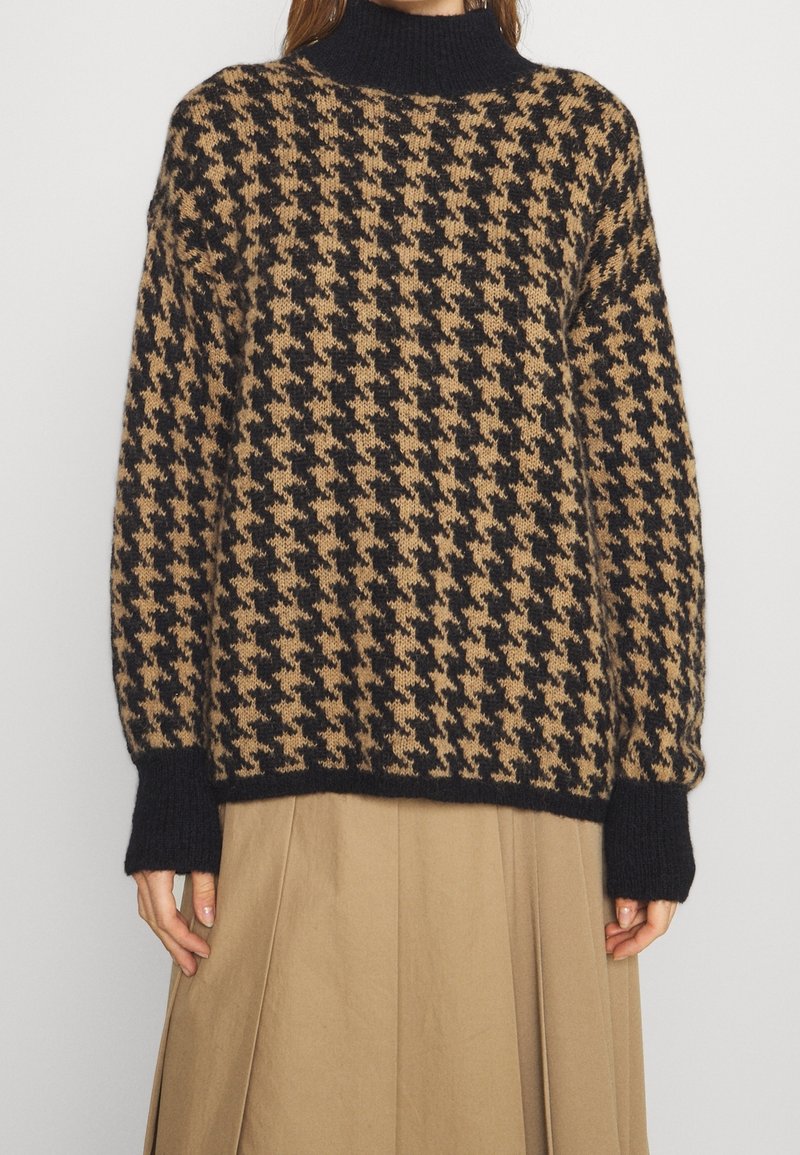 Zwart- en tan houndstooth gebreide trui met geribde manchetten en zoom, gedragen met een beige geplooide rok.