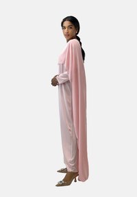 Robe en satin rose pâle avec des manches longues et un superposé fluide de type cape, assortie à des talons beige clair avec des accents décoratifs.