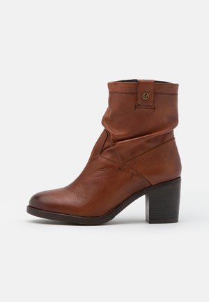 Bruine leren enkelboot met een slouchy ontwerp, ronde neus en een gestapelde hak. Bevat een gestikt accent en een klein logo-detail aan de zijkant.