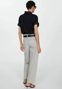 Svart skjorta med uppvikta ärmar, grå vida jeans, svart bälte och sandaler. Tyget har en jämn textur och en avslappnad design.