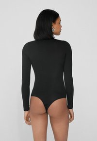 Černý body s dlouhým rukávem a vysokým výstřihem, s hlubokým výstřihem na zádech. Vyrobeno z hladkého materiálu, má přiléhavý střih a minimální detaily.