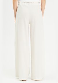 Pantalons à jambes larges en tissu crème doux et texturé avec une taille élastique, reposant au sol, présentant une finition soignée à l'ourlet.