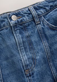 Nahaufnahme des Bunds einer blauen Jeans aus Denim mit Metallknopf, Gürtelöse und Details der Naht an der vorderen Tasche.