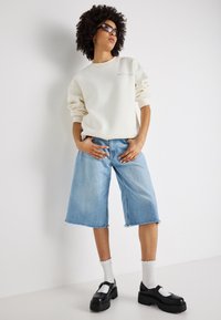 Krémová mikina se staženými rukávy, zkombinovaná se světle modrými denimovými culottes. Černé platformové boty, bílé ponožky s vlnkovaným okrajem.