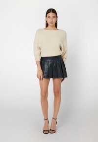 Bežinis, tekstūruotas megztinis su plačiais, užlenktais rankovėmis. Suderintas su juoda odine mini sijonu su klostėmis ir raišteliu juosmens srityje.