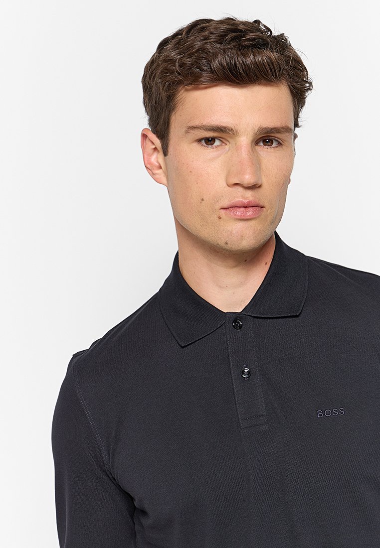 Donkergrijze poloshirt met een kraag, voorzien van een knoopsluiting met drie knopen en een subtiel geborduurd logo op de linkerkant van de borst. Soepele textuur.