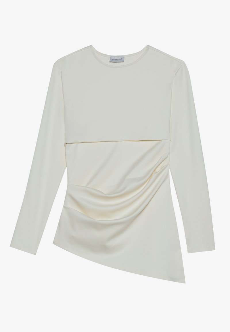 Kremowa bluzka z długim rękawem i okrągłym dekoltem, z warstwowym krojem i marszczonym detalem w dolnej części. Miękki materiał o gładkiej fakturze.