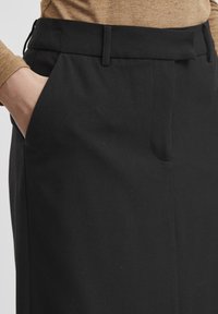 Pantalons noirs sur mesure avec une texture lisse, présentant une taille plate, des poches latérales et une ceinture structurée.