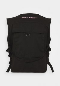 Svart tygryggsäck med en stor främre ficka med klaff, cirkulär hardwaredetalj och "NIGHT ADDICT"-text i rosa på baksidan.