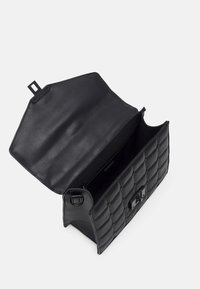 Mustaksi quiltattua nahkaa oleva käsilaukku avattuna, jossa on vetoketjullinen sisäosasto ja magneettisuljettavalla läpällä valkoista taustaa vasten.