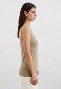 Beige Tanktop mit taillierter Passform, aus glattem Stoff gefertigt. Verfügt über schmale Träger und einen runden Ausschnitt. Einfach und schnörkellos.