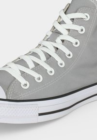 Γκρι πάνινο sneaker ψηλού τύπου με λευκά κορδόνια, λευκή λαστιχένια μύτη και λευκή σόλα με μαύρη ρίγα.