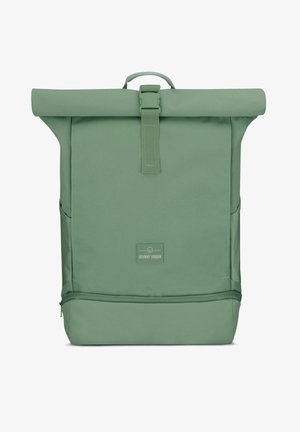 Rucsac verde cu capac pliabil, cu o formă plată, fabricat dintr-un material durabil, având o închidere cu curea în față, buzunare laterale și un patch cu logo.