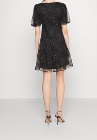 Robe noire avec des manches ballon transparentes, motif floral brodé, ourlet évasé et taille cintrée. Associée à des sandales à talons hauts à lanières.