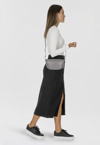 Borsa a tracolla grigia con un design curvo e cerniera argentata, indossata con un top a maniche lunghe fitted bianco e una gonna di jeans nera.