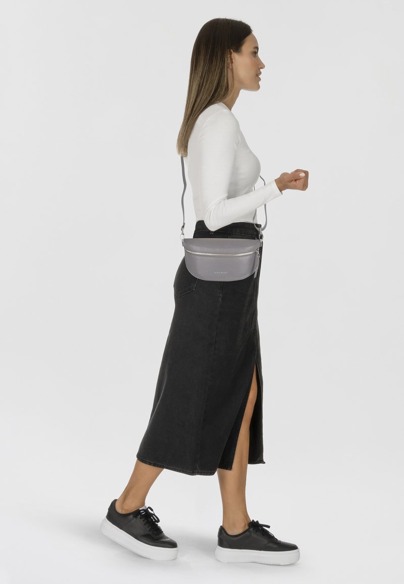 Borsa a tracolla grigia con un design curvo e cerniera argentata, indossata con un top a maniche lunghe fitted bianco e una gonna di jeans nera.