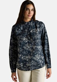 Langärmlige Bluse mit einem dunkelblauen Hintergrund und weißen botanischen und tierischen Druck. Hat einen Rüschenausschnitt und Knopfdetails.