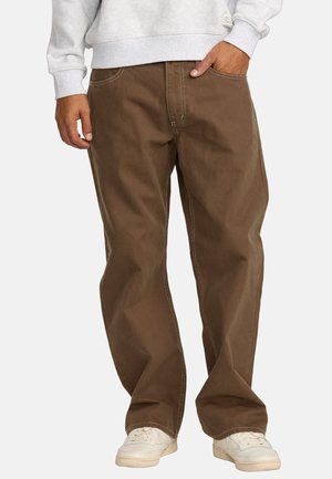 Brown straight-leg pants in sturdy cotton. Features white stitching and side pockets. Worn with a light gray sweatshirt and white sneakers.