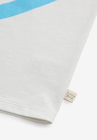 Weißes Baumwoll-T-Shirt mit einem blauen, geschwungenen Streifen. Mit aufgerollten Ärmeln und einem kleinen "Little Bird"-Label am Saum gefertigt.