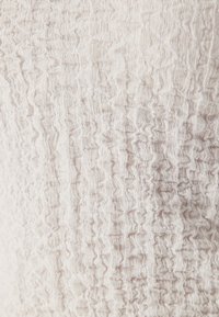 Tissu texturé beige clair avec un motif froissé, présentant des vagues et des crêtes irrégulières sur toute la surface.