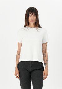 Witte t-shirt met korte mouwen en een ronde halslijn, gemaakt van gladde stof. Zwarte jeans met een rechte snit. Minimale details en geen zichtbare patronen.