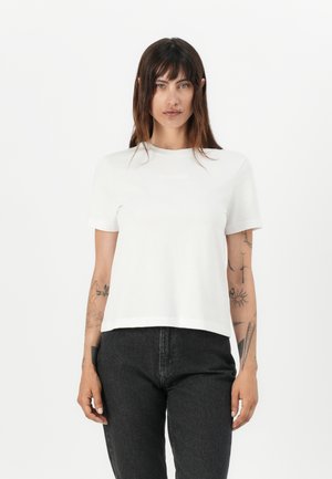 Hvit T-skjorte med kort erme og rund hals, laget av glatt stoff. Sorte jeans med rett kutt. Minimal detaljering og ingen synlige mønstre.