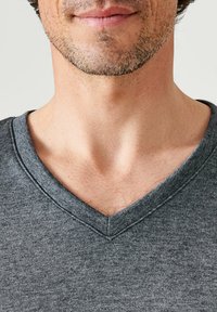 Grijze v-hals t-shirt van zacht materiaal. Heeft een eenvoudig, effen ontwerp met een gestructureerd oppervlak en versterkte stiksels langs de halslijn.