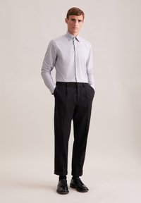 Camicetta grigia chiara aderente con colletto, taschino sul petto; pantaloni scuri plissettati con risvolti; scarpe eleganti in pelle nera.