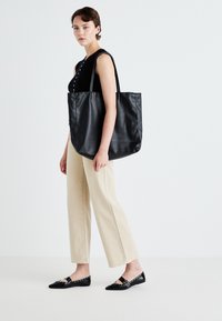 Svart läder tote-väska med två långa handtag, slät textur och rymlig design; bärs tillsammans med avslappnade beiga vida byxor och svarta ballerinas.