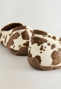 Pantoffels met een getextureerd patroon van wit en bruin koeienhuid, met een ronde vorm en een bruine rubberen zool.