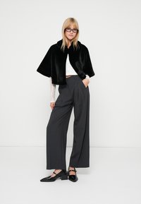 Črna umetna krznena kratka plaščica preko bele čipkaste majice, v kombinaciji z sivo visokim pasom hlačami in črnimi čevlji z visokimi petami. Minimalističen dizajn.