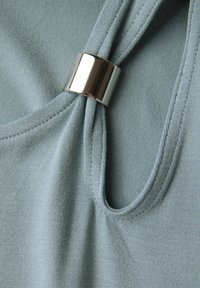 Lichtblauwe stoffen top met een geplooid detail bij de hals dat vastgemaakt is met een glanzende metalen ring. Zachte textuur met zichtbare stiksels.