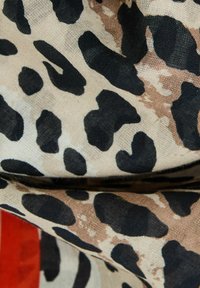 Tejido beige con un patrón de leopardo en negro y marrón, con una textura suave y costuras visibles. Acentuado por un borde oscuro.