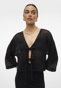 Melnas, īsā garuma mežģīņu jakas ar dziļu V-veida kakla izgriezumu, 3/4 piedurknēm un priekšējām saitēm. Komplicēti raksti ar pusei caurspīdīgu tekstūru.