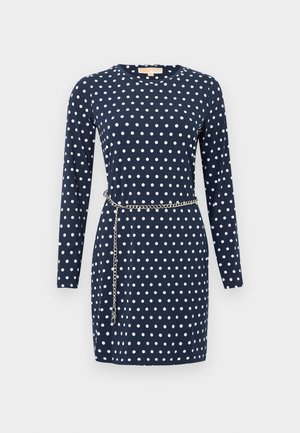Robe manches longues bleu marine à pois blancs avec une ceinture chaîne argentée drapée autour de la taille.
