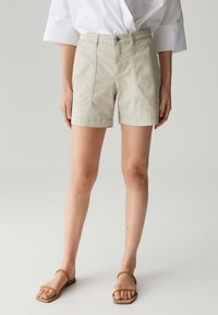 Shorts en coton beige taille haute, dotés de deux poches avant et d'une coupe droite, se terminant au-dessus du genou. Associés à des sandales plates marron.