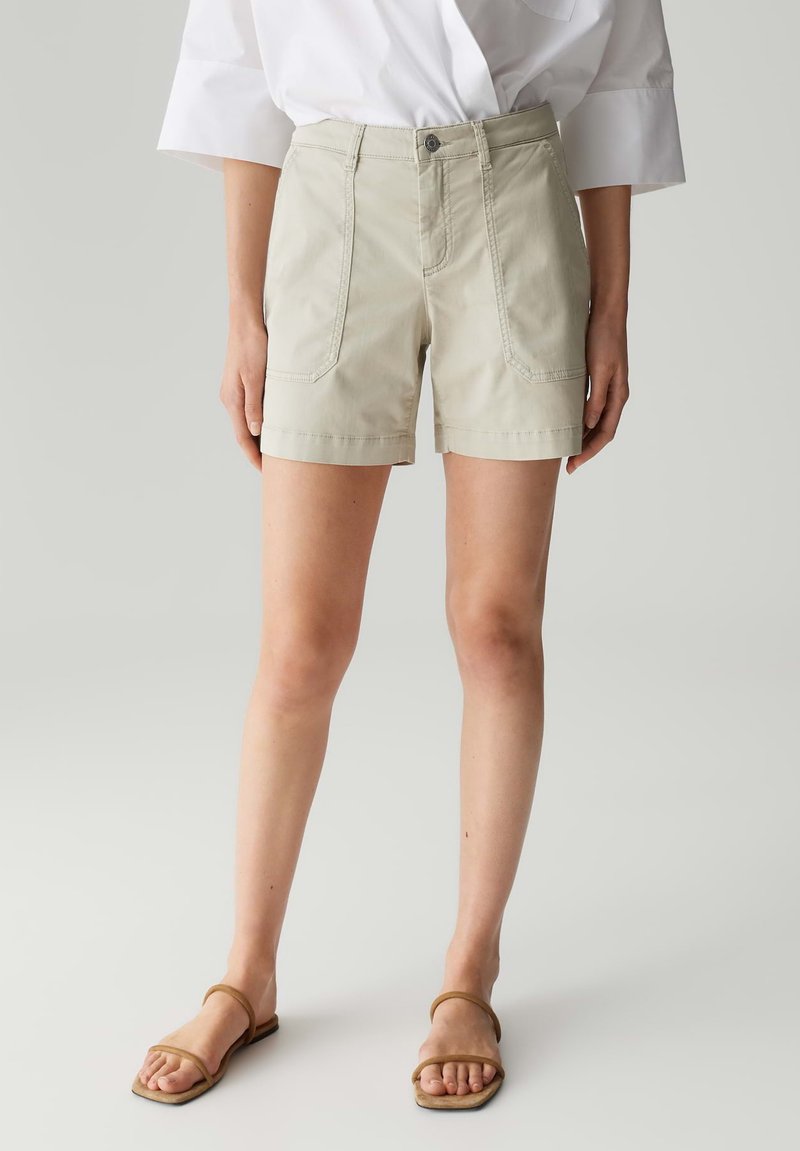 Shorts en coton beige taille haute, dotés de deux poches avant et d'une coupe droite, se terminant au-dessus du genou. Associés à des sandales plates marron.