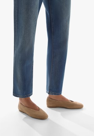 Beige suede ballerina flats with a rounded toe and cut-out detail, paired with blue, slightly cropped denim jeans.